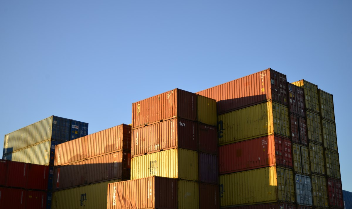Stacked shipping containers under a clear blue sky, representing international trade